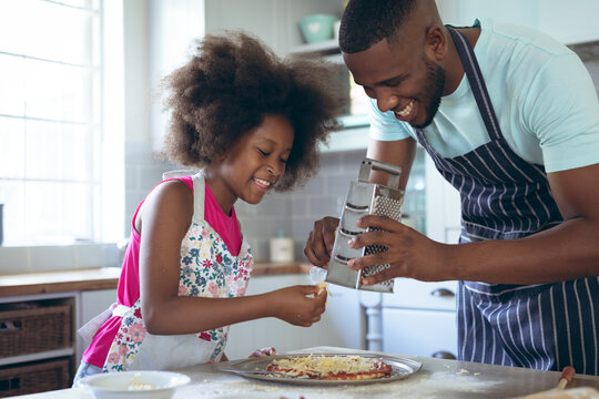 African american girl and her father making pizza together in kitchen