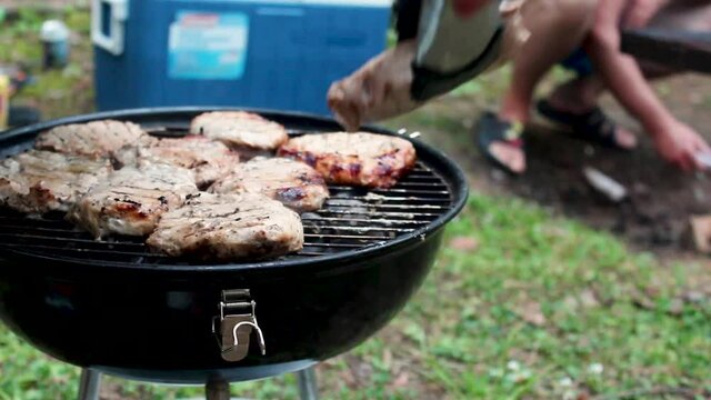 Cooking meat on red round barbecue grill bbq. Open bbq cover, rotating beaf steaks with open fire smoke. Outside in camping
