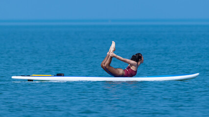 Sport woman yogini posing balancing table top practice yoga exercise on sup board on the sea in relaxing day , yoga is meditation and healthy sport concept.