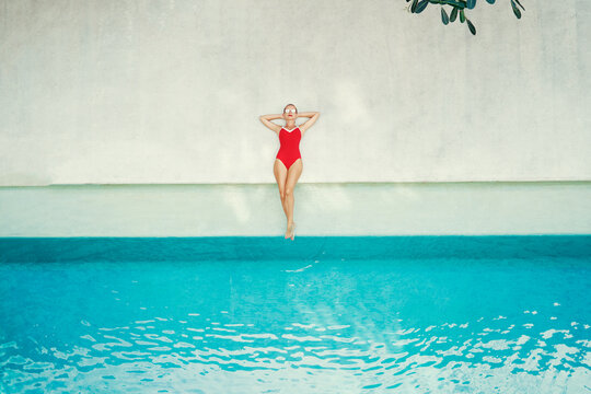 Enjoying suntan and vacation. Top view of pretty young woman in red swimsuit lying near swimming pool.