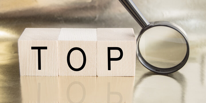 The word UP is written on wooden cubes and a magnifying glass on a gold background with reflection, TOP concept