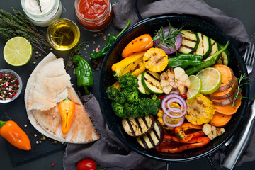 Grilled assorted vegetables in cast iron pan on black background.