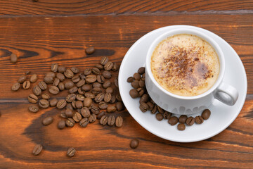 white cup with cappuccino and coffee beans on wooden background