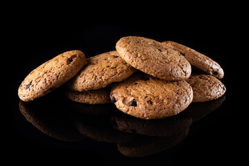 Oatmeal cookies with chocolate chips are isolated on a black background with a reflection. Lots of brown round homemade cookies lying on a reflective surface, close-up