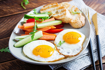 Breakfast. Fried eggs with fresh carrot, cucumber, paprika and toast on wooden background. Vegetarian meal.