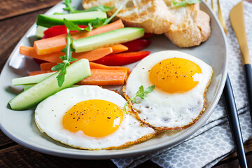 Breakfast. Fried eggs with fresh carrot, cucumber, paprika and toast on wooden background....