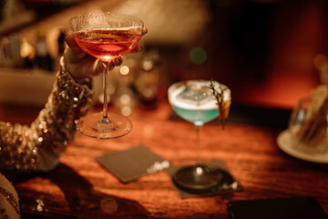 A glass of a cosmopolitan cocktail in woman`s hand in bar. Pink alcoholic cocktail