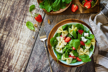 Italian pasta salad with strawberries, arugula, nuts, soft cheese dressed with balsamic sauce on the wooden table. Top view flat lay. Copy space.