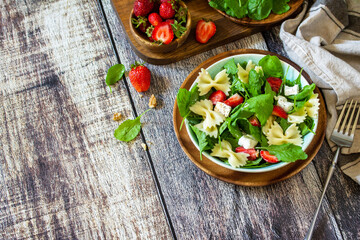 Italian pasta salad with strawberries, arugula, nuts, soft cheese dressed with balsamic sauce on the wooden table. Copy space.