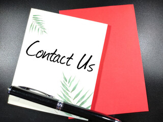 Word CONTACT US on notepad with pen and black background.Business concept.