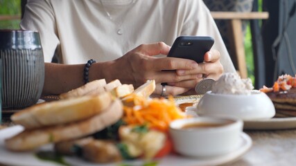 Hands browsing on the phone on the background in the focus. Blurred foreground with the breakfast