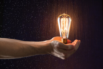 hand holds in the air a burning vintage light bulb without wires