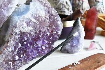 A close up image of burning incense stick with several amethyst crystals on a white table top. 