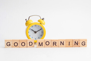 Yellow alarm clock with bell and Good Morning text from wooden cubes.