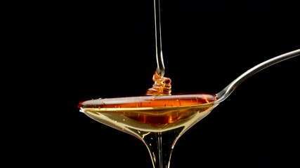 Liquid golden honey is poured onto a steel spoon on a black isolated background, slow motion - Powered by Adobe