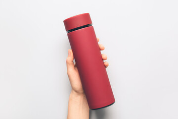 Female hand with modern thermos on light background