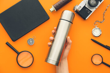 Female hand with modern thermos and items for travel on color background