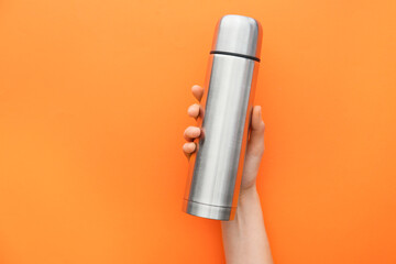 Female hand with thermos flask on color background