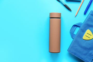 Modern thermos, schoolbag and stationery on color background