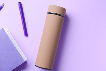 Modern thermos, notebook and pens on color background