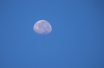 Three quarter moon isolated hanging in a blue daylight sky image for background use