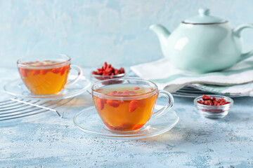 Glass cups of hot tea with goji berries on color background