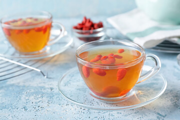 Glass cups of hot tea with goji berries on color background
