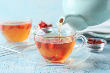 Pouring tasty tea with goji berries from teapot into glass cup on table