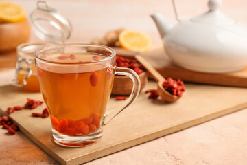 Glass cup of hot tea with goji berries and honey on color background