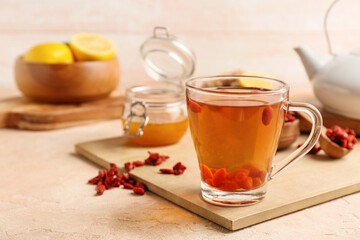 Glass cup of hot tea with goji berries and honey on color background