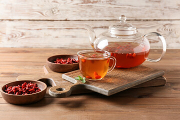 Teapot and glass cup of hot tea with goji berries on wooden background