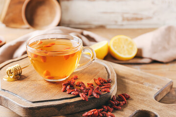 Glass cup of hot tea with goji berries on light wooden background