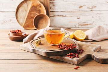 Glass cup of hot tea with goji berries on light wooden background