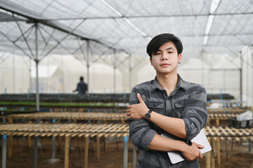 Asian farmer man standing with crossed arms standing in greenhouse.
