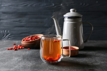 Teapot and glass cup of hot tea with goji berries on dark background