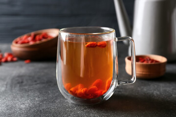 Teapot and glass cup of hot tea with goji berries on dark background