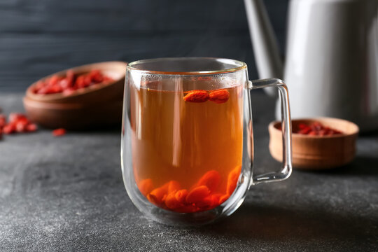 Teapot and glass cup of hot tea with goji berries on dark background