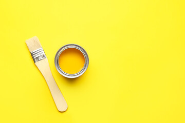 Can of yellow paint and brush on color background