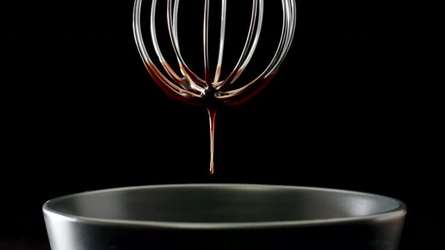 Last drop of liquid chocolate is dripping from steel whisk on black background