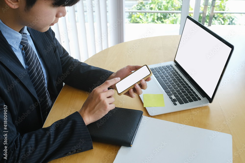 Wall mural Confident businessman using smart phone and working with laptop computer at office desk.