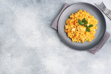 Delicious Asian pilaf, stewed rice with vegetables and chicken on a plate. gray concrete background. copy space.