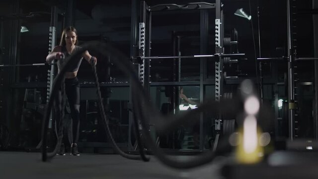 Healthy lifestyle, female performs exercises with battle ropes, endurance training in the gym, 4k slow motion.