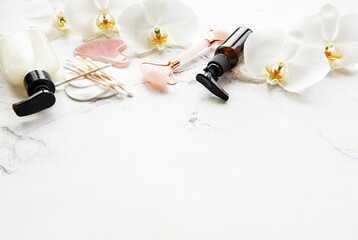 Face massage jade roller with cosmetic product on white marble background