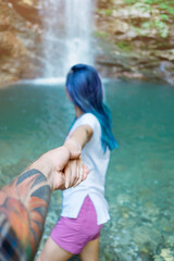 Young woman holding man's hand and leading him to waterfall, point of view. Focus on hand. Back view.