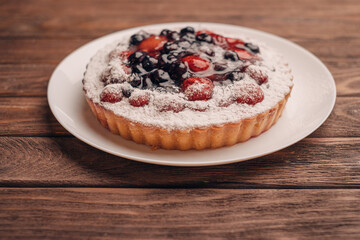 Berry pie on a saucer on a wooden table.