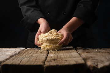 Cooking dough with the hands of a chef for homemade bread, pizza, pasta recipe.On a black background for design, with space for design.Horizontal photo, cooking and gastronomy