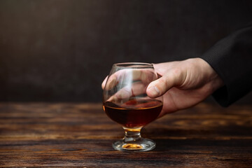 a man holds a glass of cognac on a dark background on a wooden table in front of him . the concept of alcoholism