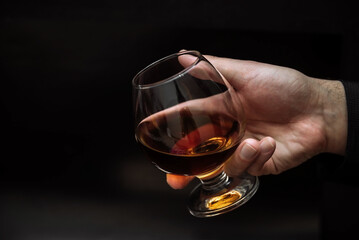 a man holds a glass of cognac on a dark background on a wooden table in front of him . the concept...
