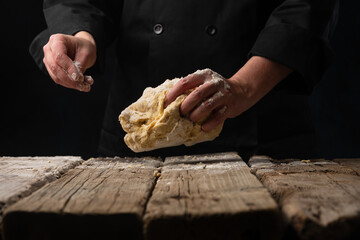 The dough in the hand of the chef on a dark black wood background. Baking bread, pizza, pasta. A recipe from the chef for pizza, bread or pastries. Home kitchen with space for text for menu design