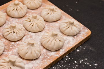 Smooth rows of raw Georgian khinkali crushed by flour lying on the corner of a wooden board